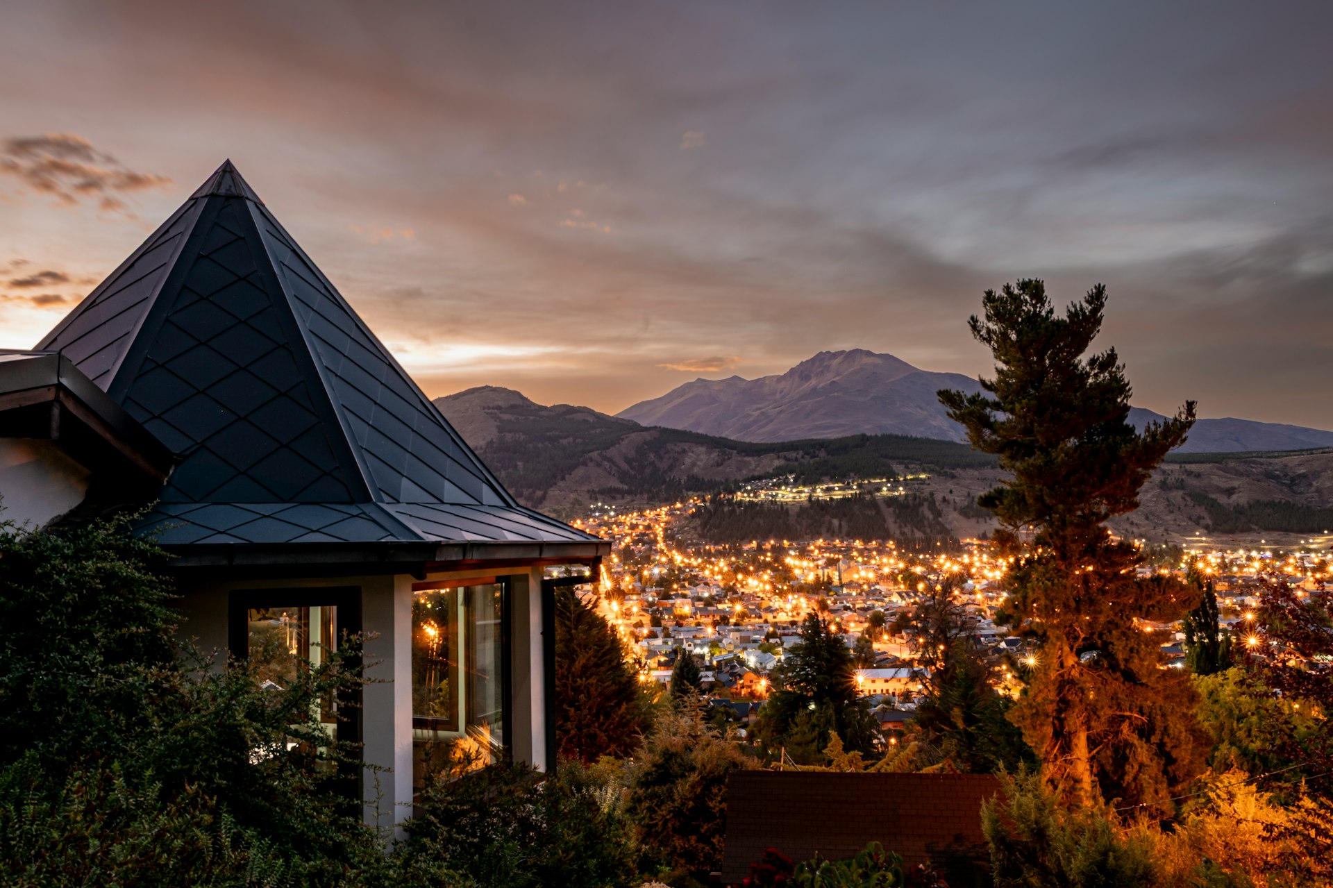 A town lights up at dusk with mountains in background
